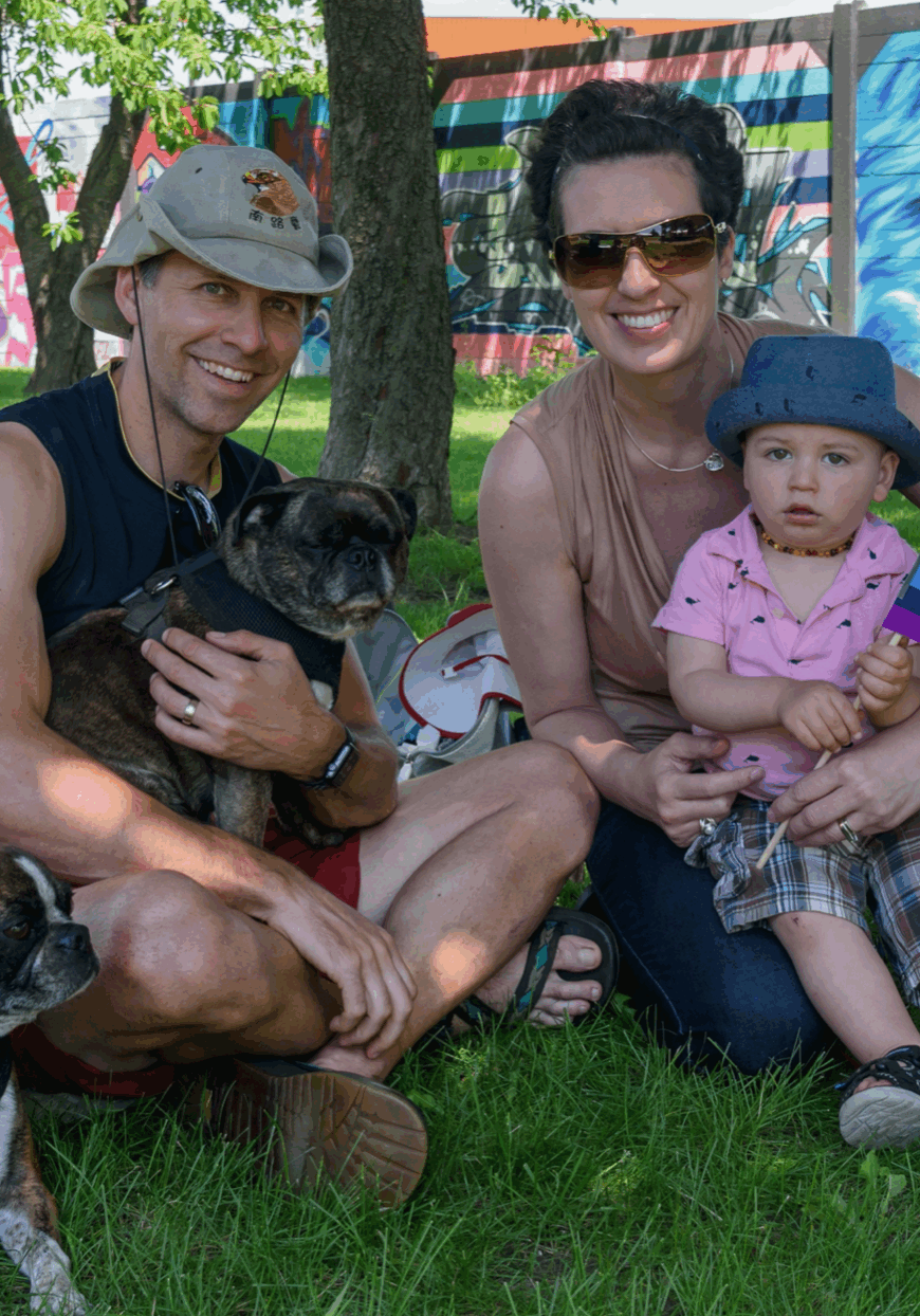 family of 3, 2 adults, 1 toddler, and 2 dogs, siting under a tree